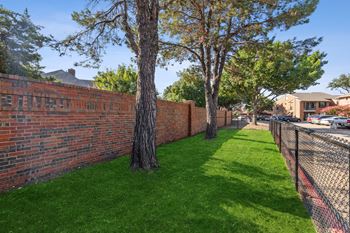A brick retaining wall with trees and a chain link fence